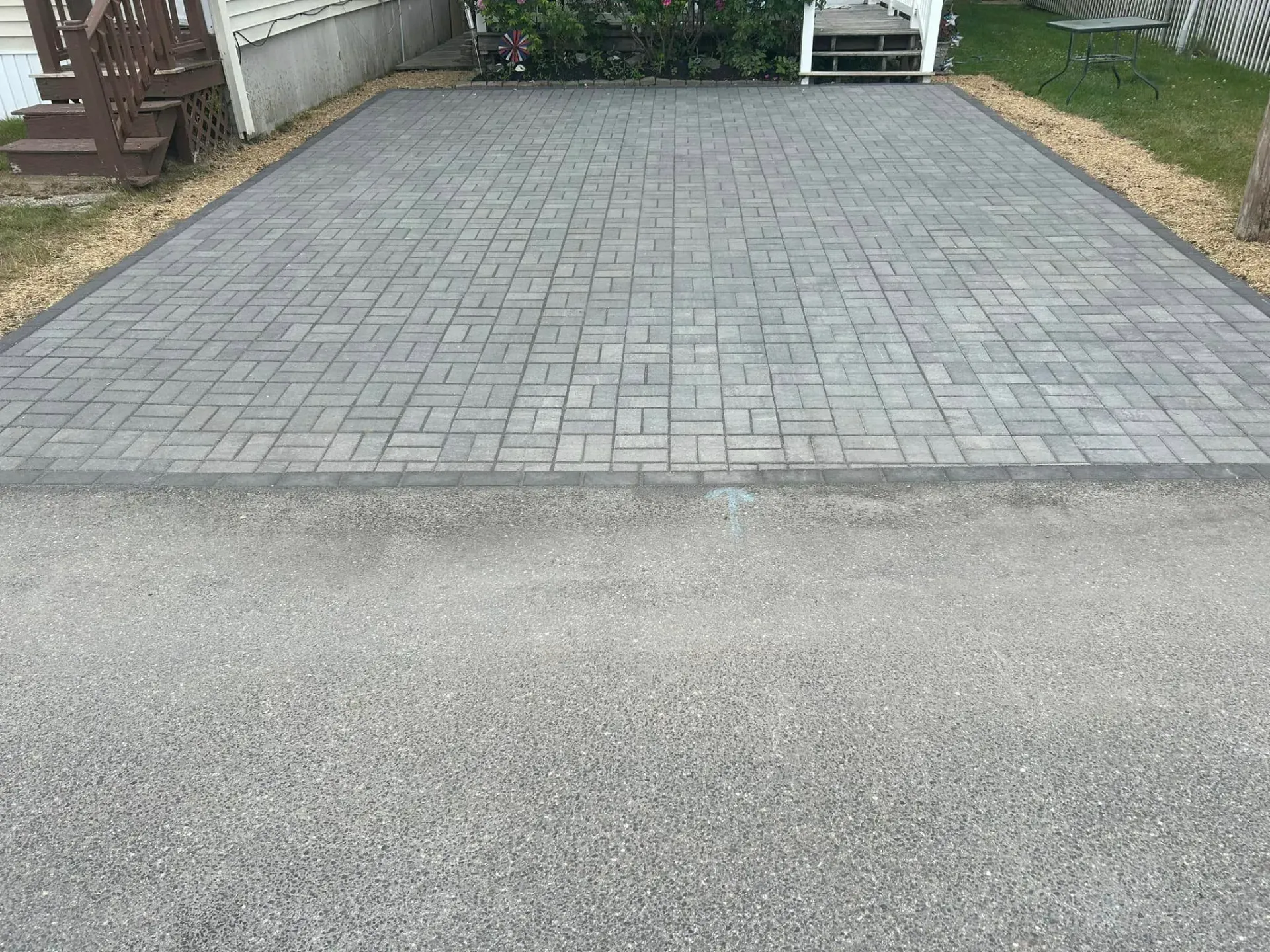 A brick driveway with a bench in the background and a house in the background.