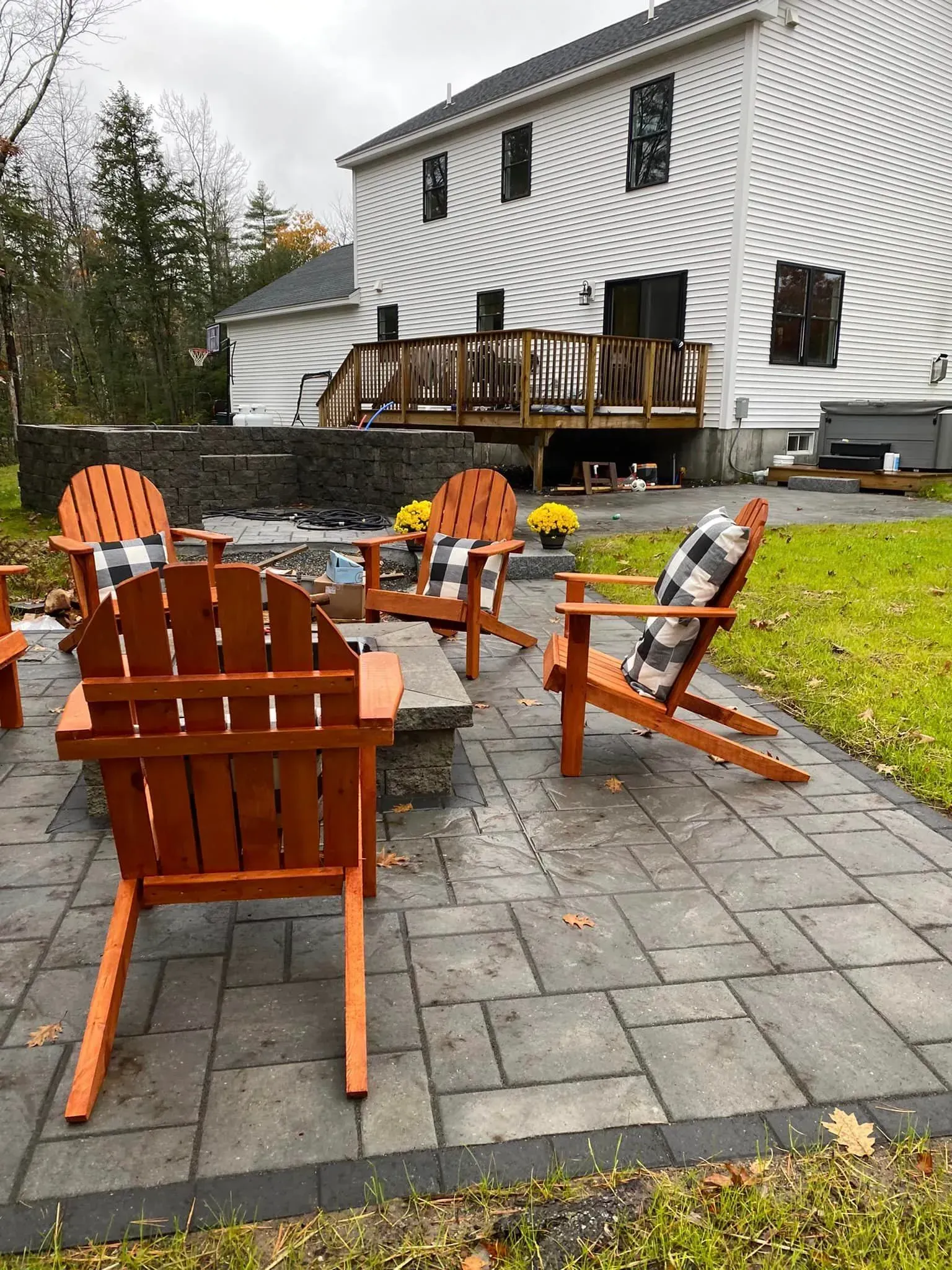A patio with wooden chairs and a fire pit in front of a house.