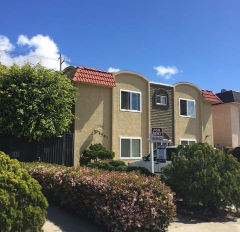 Two story apartment building with landscaping; it's a mostly clear sunny day