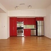 Apartment kitchen with stainless steel appliances and red cabinets; hardwood flooring