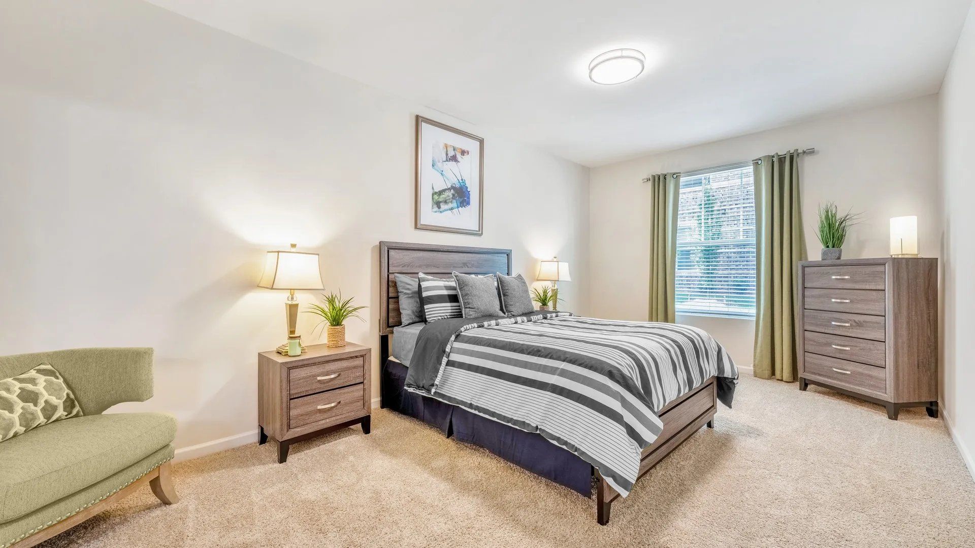 A well-decorated bedroom featuring a bed with striped bedding, a nightstand with a lamp, and a window with natural light
