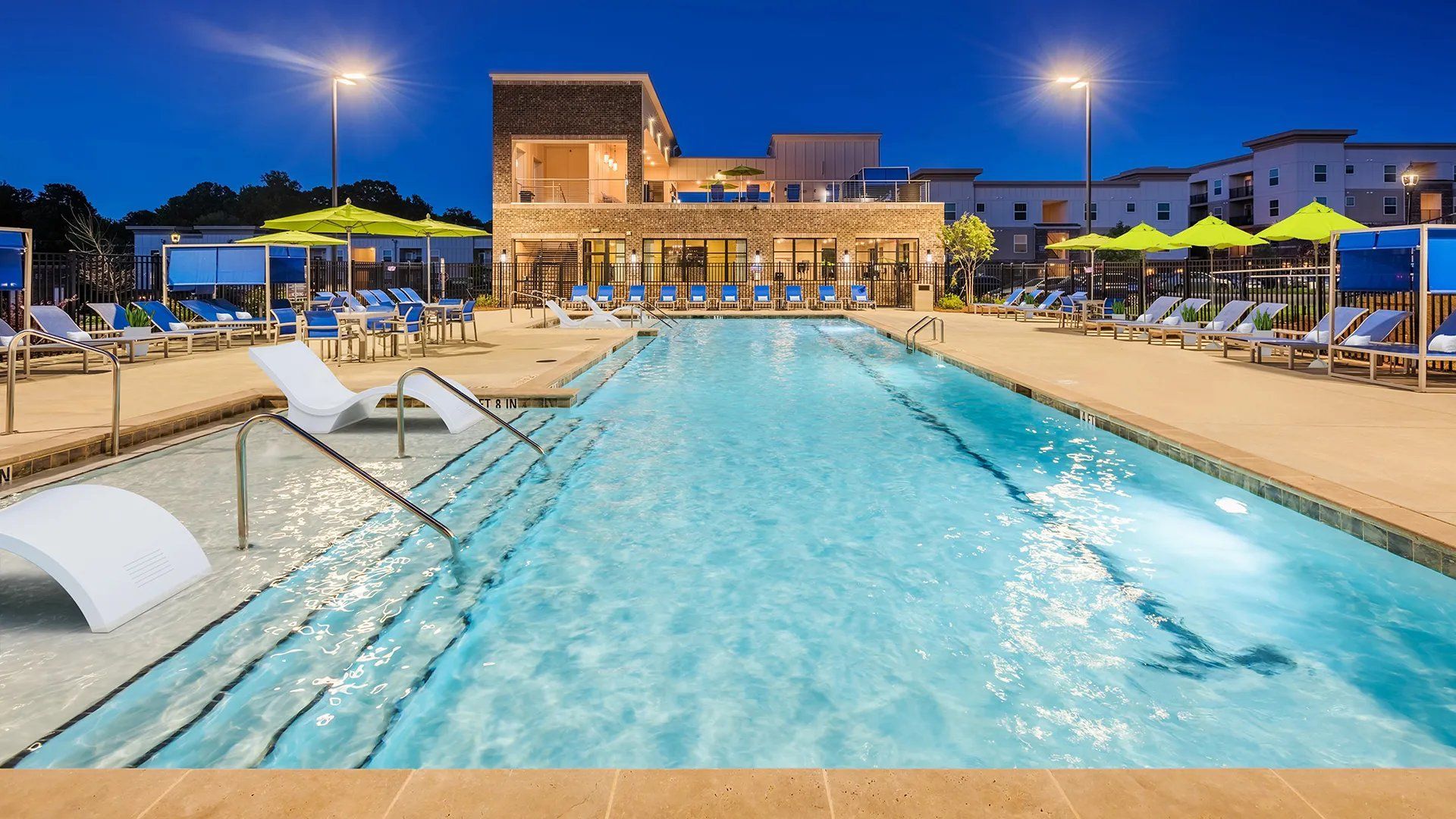 Community pool area with lounge chairs and vibrant umbrellas at night.