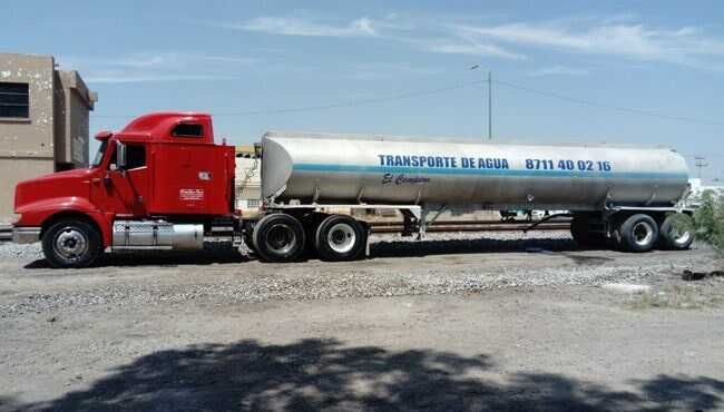 Un camión rojo con un tanque blanco en la parte trasera está estacionado en un estacionamiento.