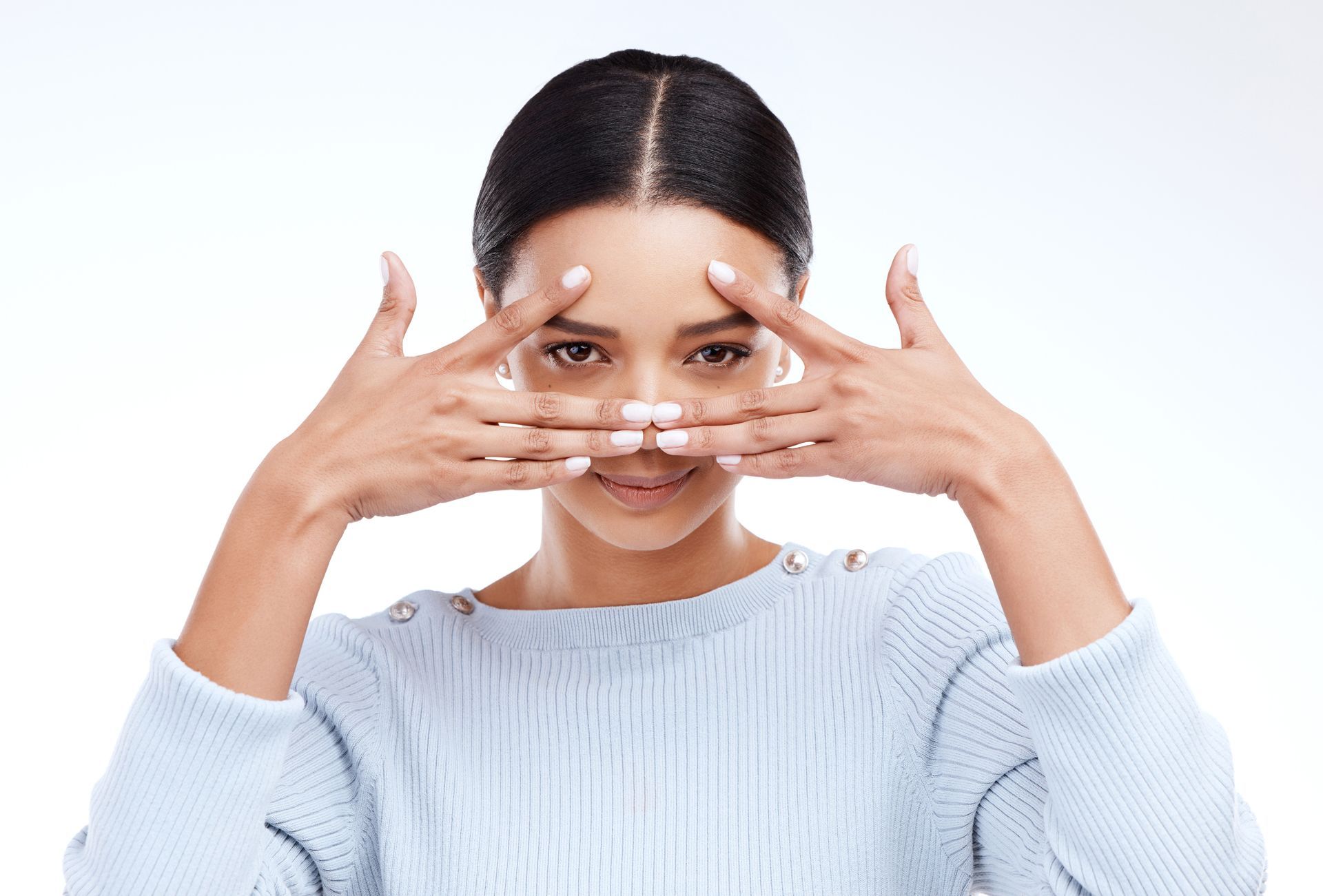 A woman in a blue sweater is covering her eyes with her hands.