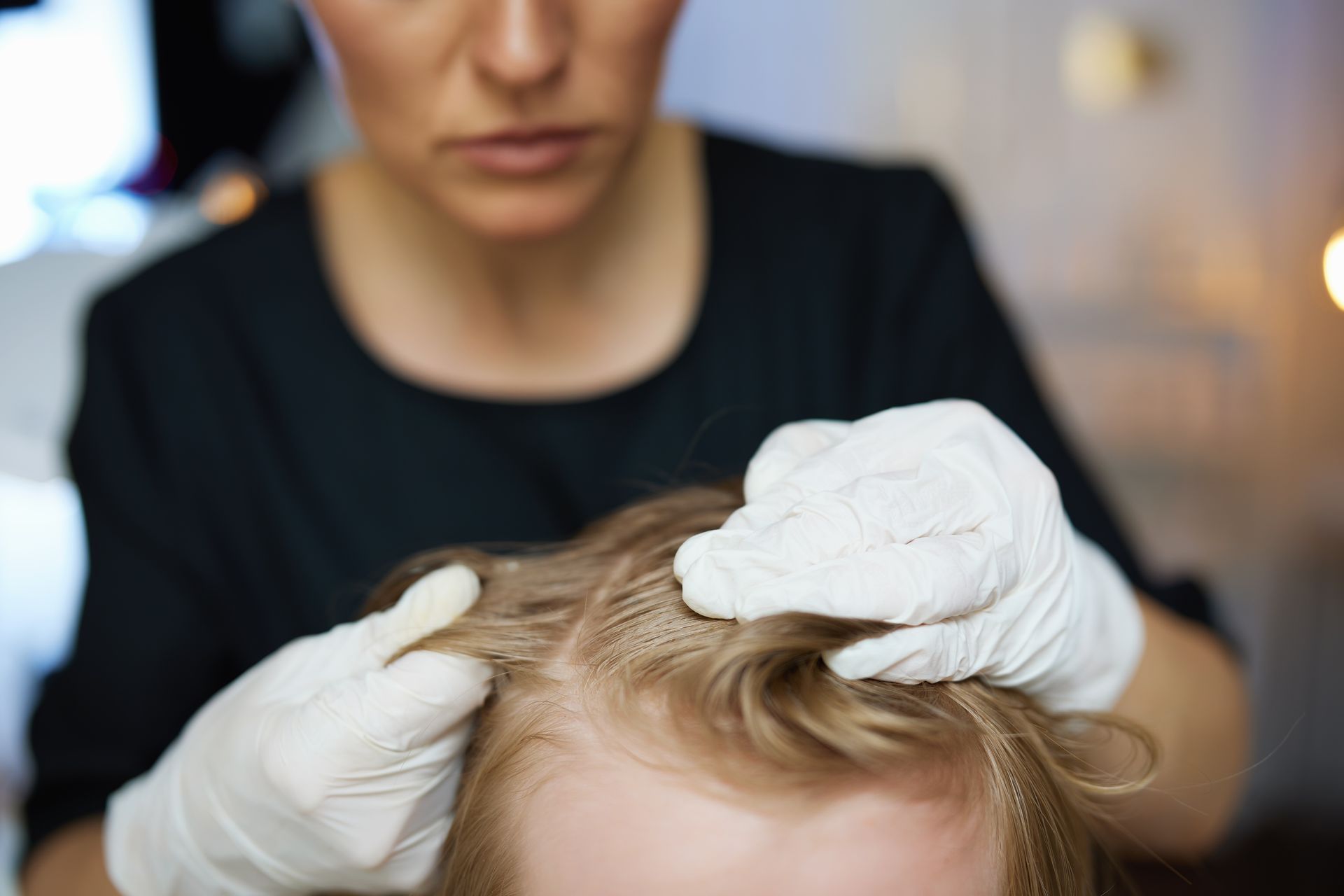 A professional in white gloves examines a person's scalp and hair.