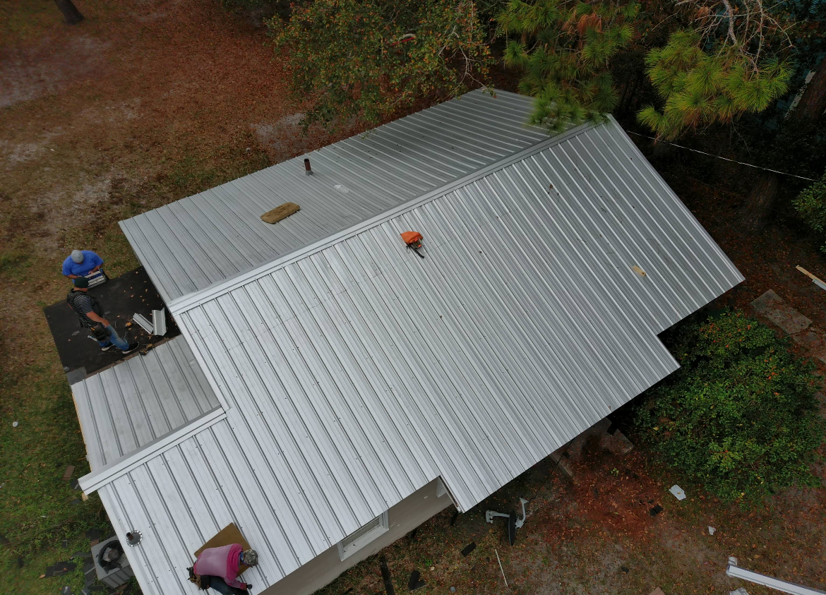 Overhead view of a house with a new, silver metal roof. A person works on the roof.
