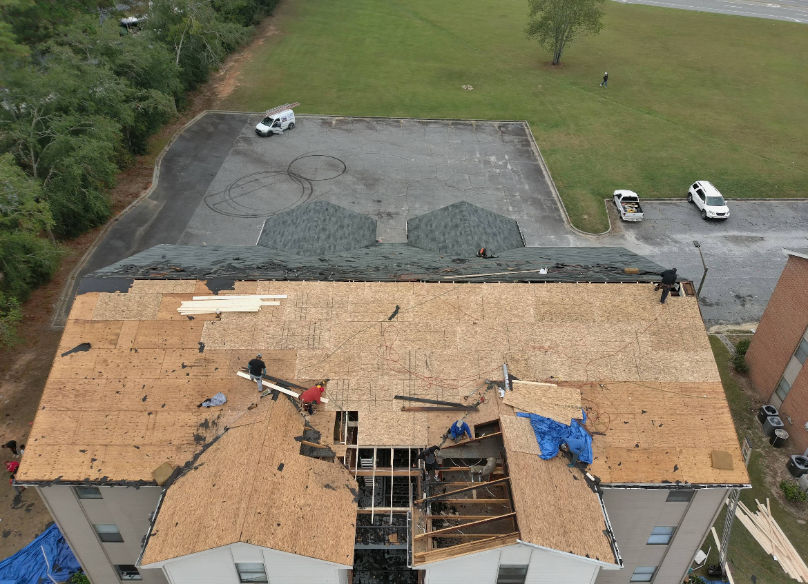 Aerial view of a building roof under construction; workers on roof with exposed structure and new sheathing.