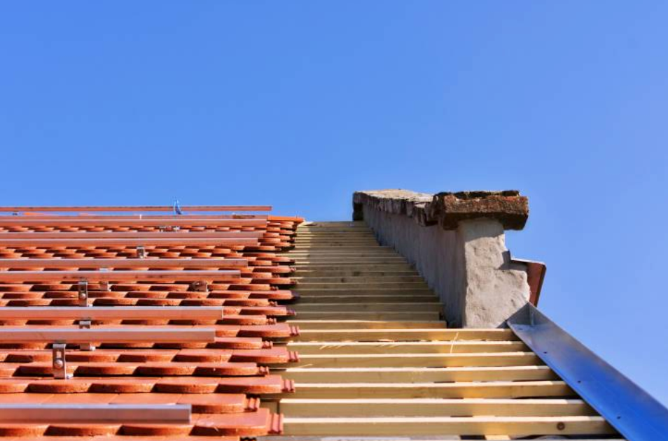 Roof partially covered with red tiles, other half exposed with white underlayment against a blue sky.