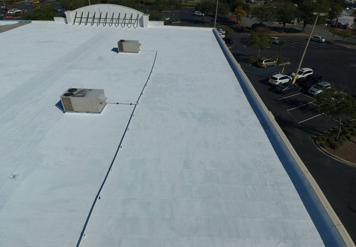 Aerial view of a white commercial building roof with HVAC units and a parking lot.