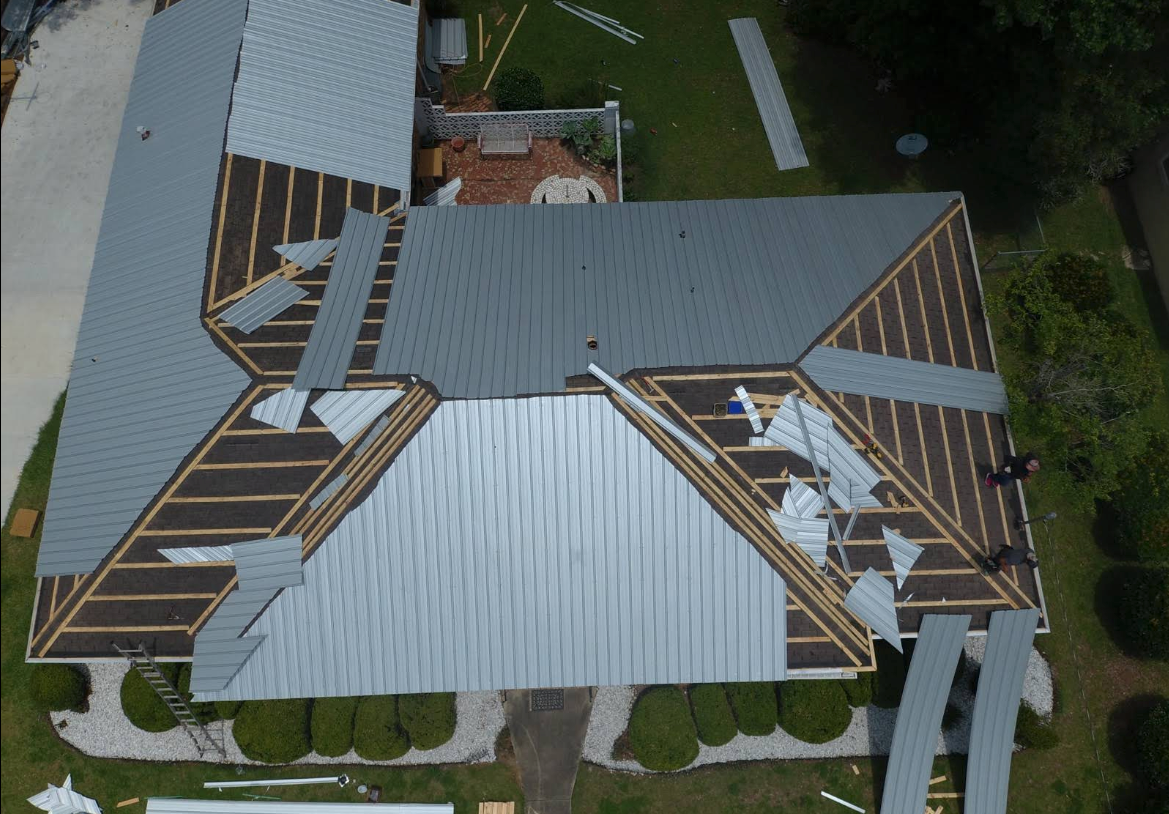 Overhead view of a house roof partially covered with gray shingles and exposed wooden beams; construction in progress.