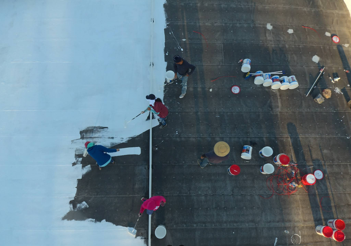 People painting a white line on a dark surface, with buckets of paint and supplies scattered around.