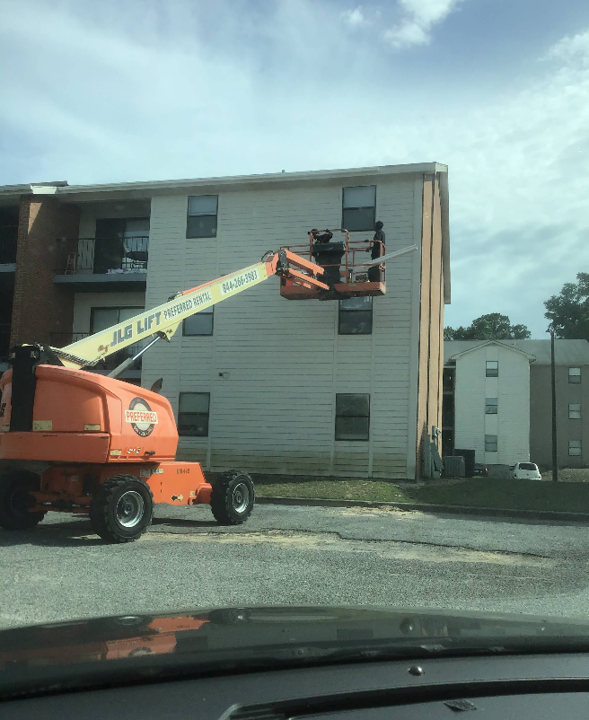 An orange JLG lift with two workers near a building's roof; the lift is in use.