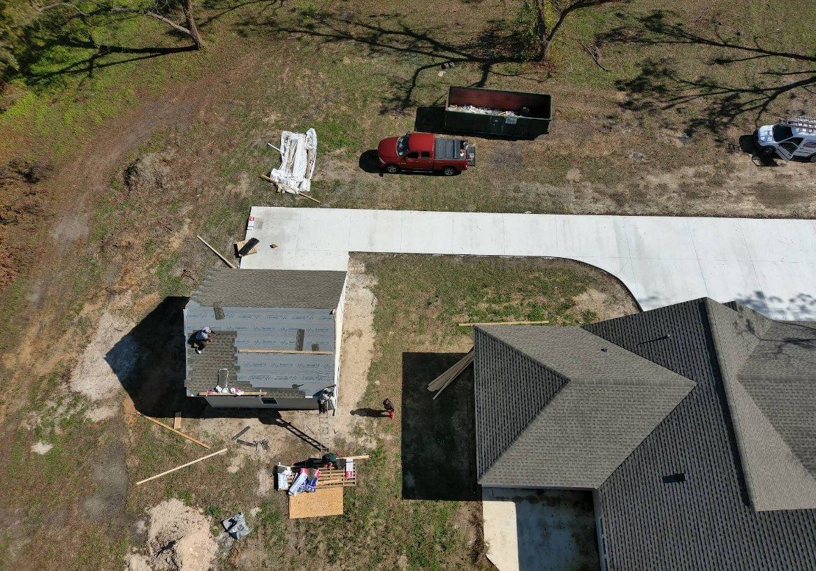 Aerial view of a house undergoing roof repair; a pickup truck, dumpster, and supplies are also present.