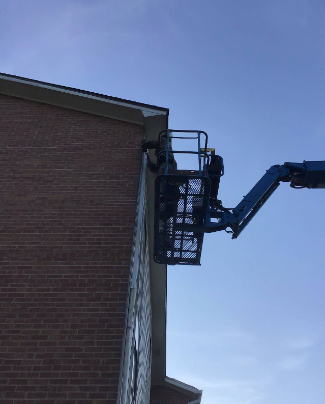 Person in a lift basket working on the side of a brick building.
