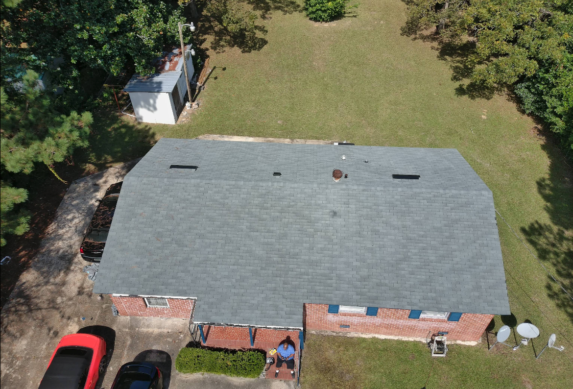 Overhead view of house with gray roof, red brick facade, two cars, and a shed in a grassy yard.