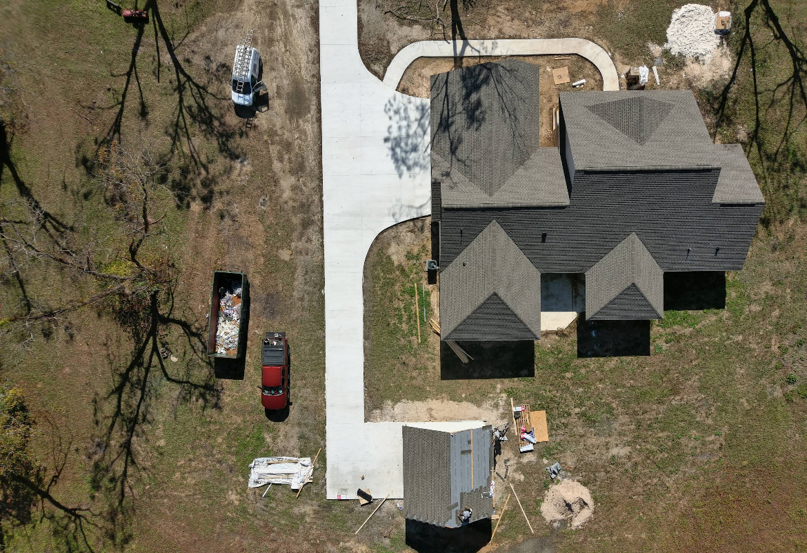 Aerial view of a house under construction with a long, curved driveway and a shed.