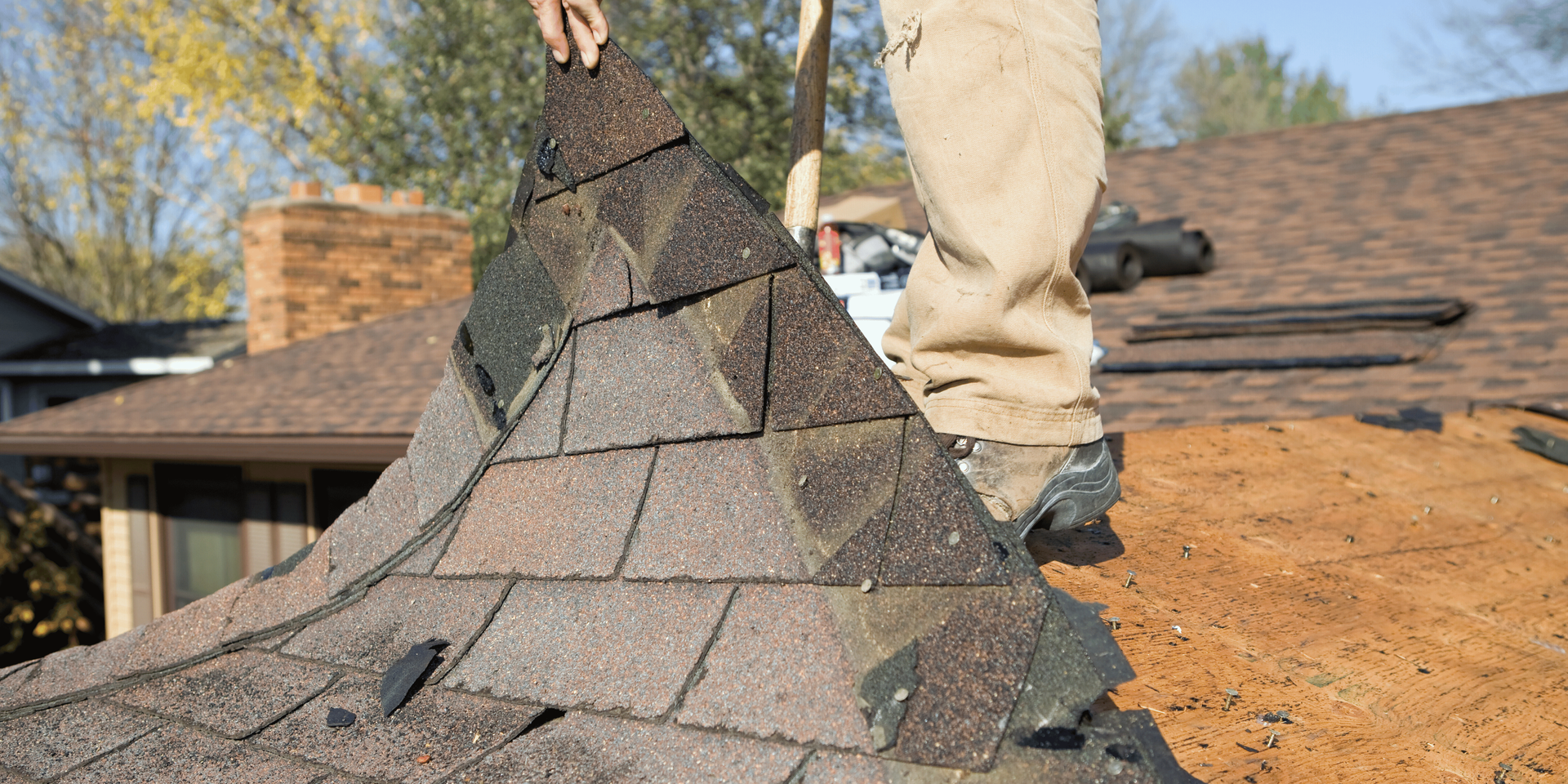 Person on a roof removing shingles from a chimney.