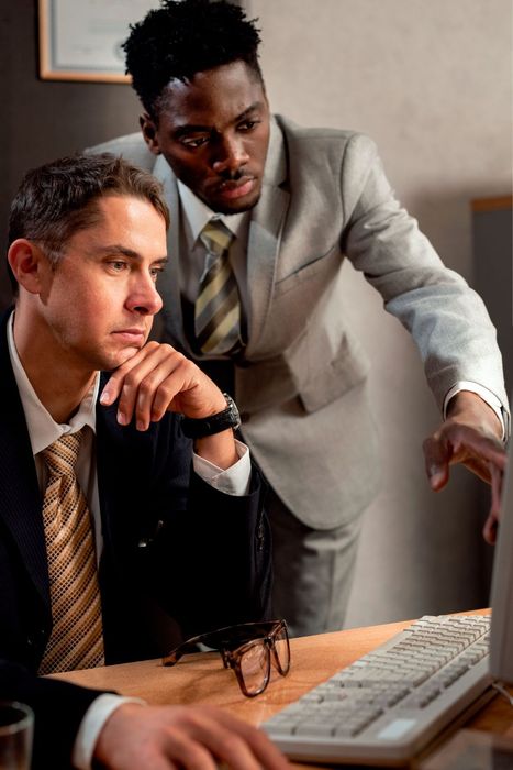 Two men in suits and ties are looking at a computer screen.