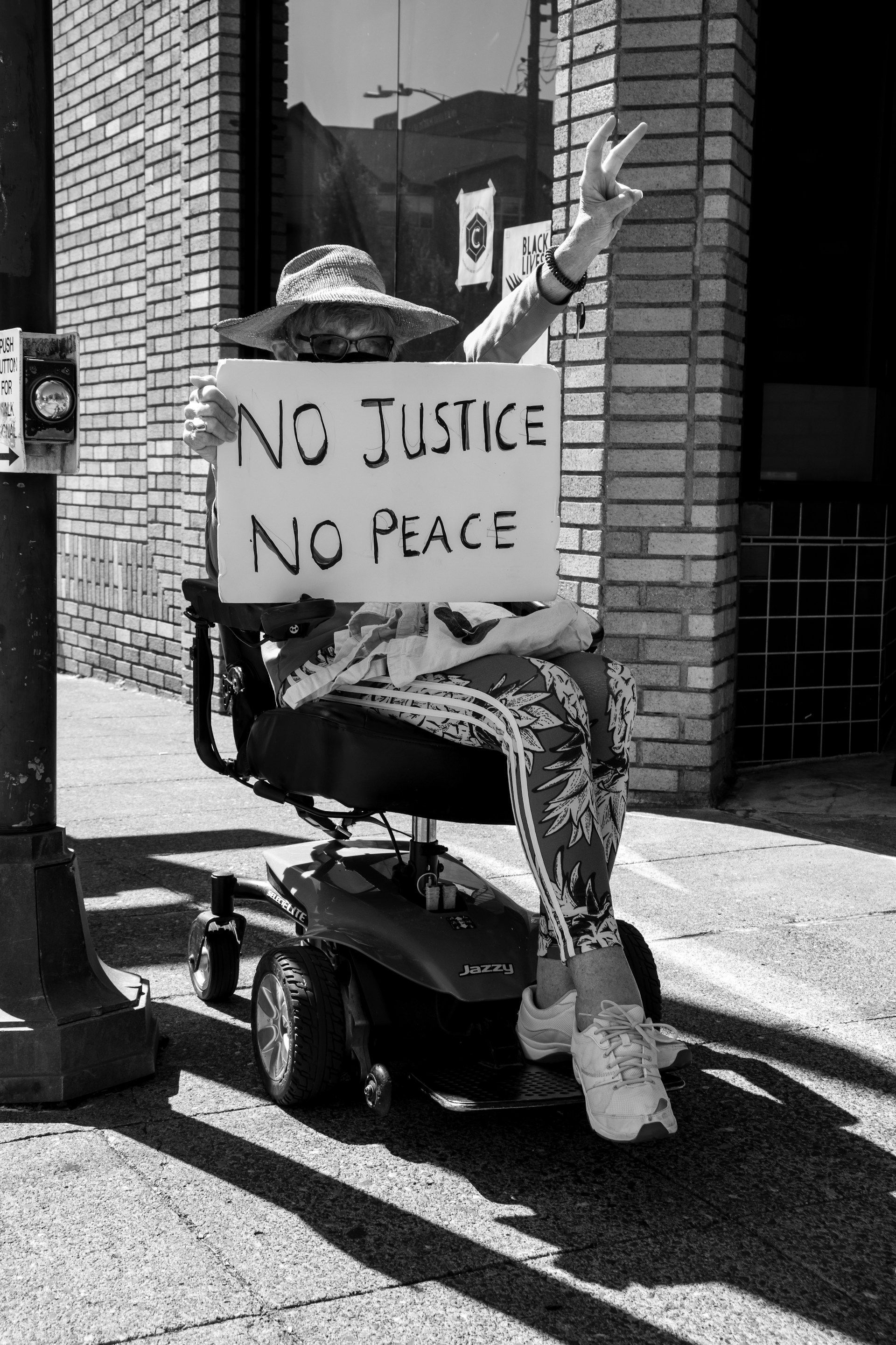 A woman in a wheelchair is holding a sign that says no justice no peace