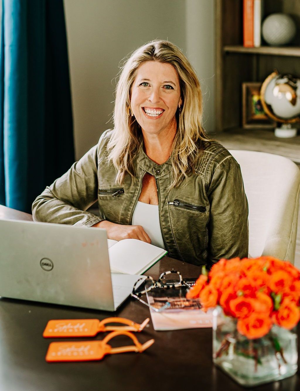A woman is sitting at a desk with a laptop and a vase of flowers.