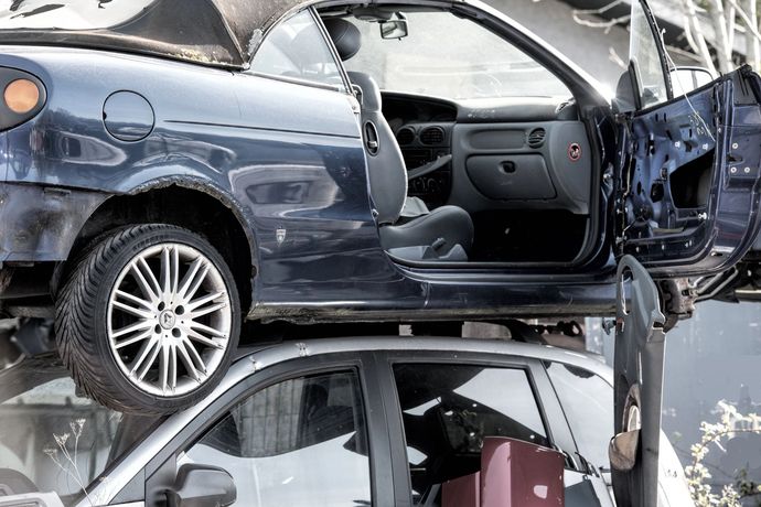 In un deposito di rottami, un'auto blu scuro è impilata sopra un'auto argentata.