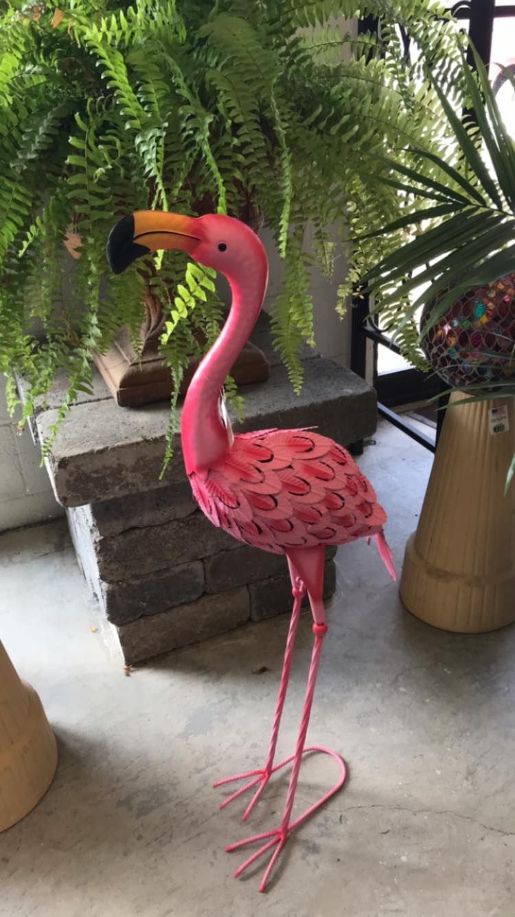 A pink flamingo statue is standing next to a potted plant.