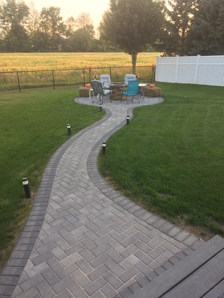 A brick walkway leading to a fire pit in a backyard
