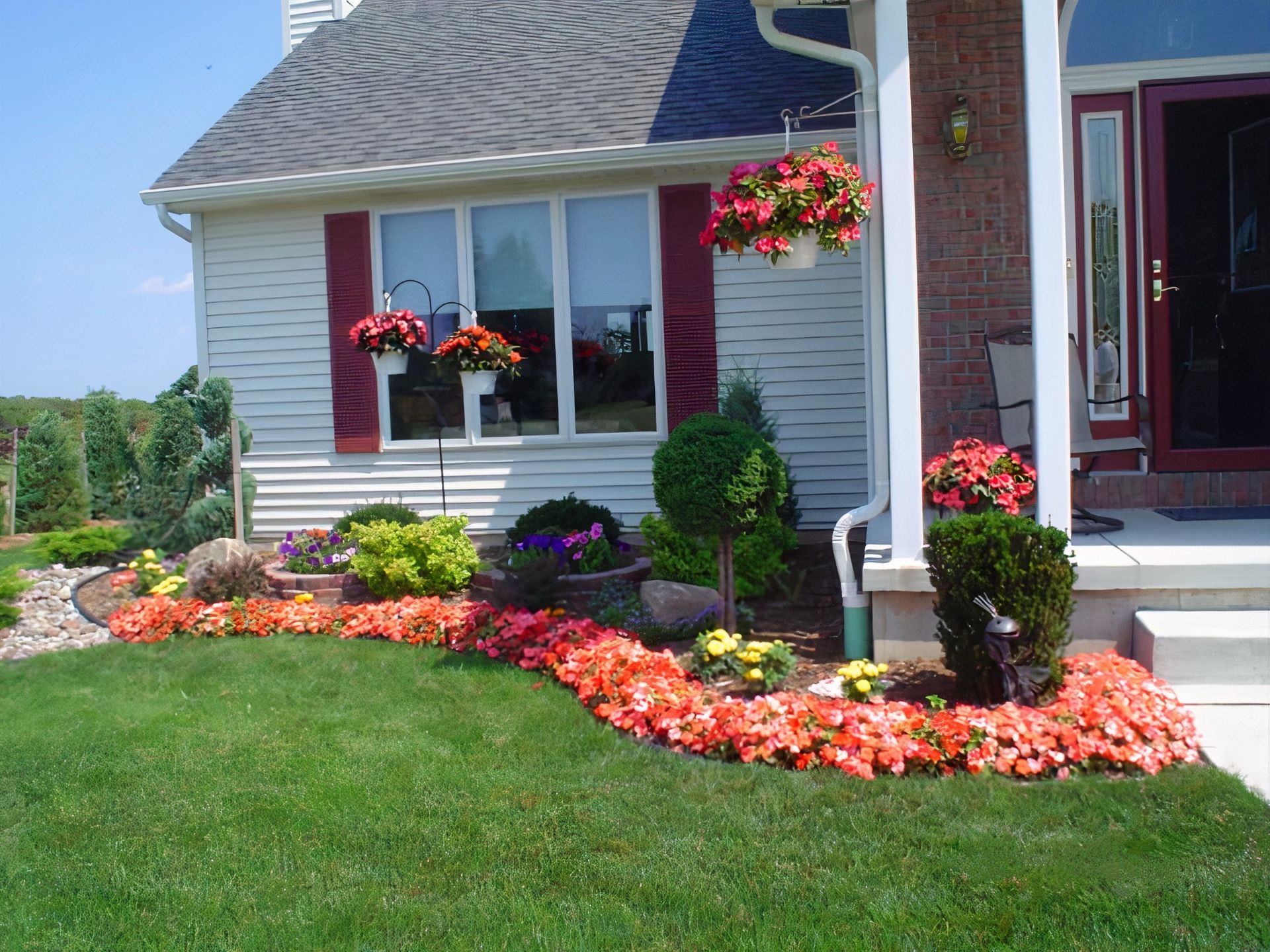 A white house with red shutters and flowers in front of it