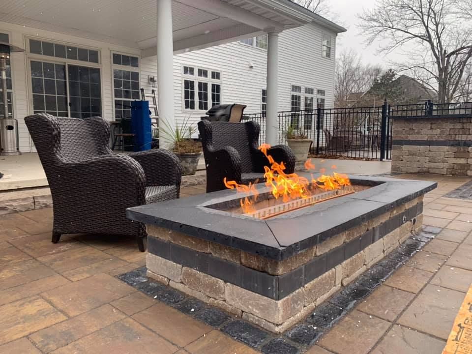 A fire pit on a patio with chairs and a house in the background.