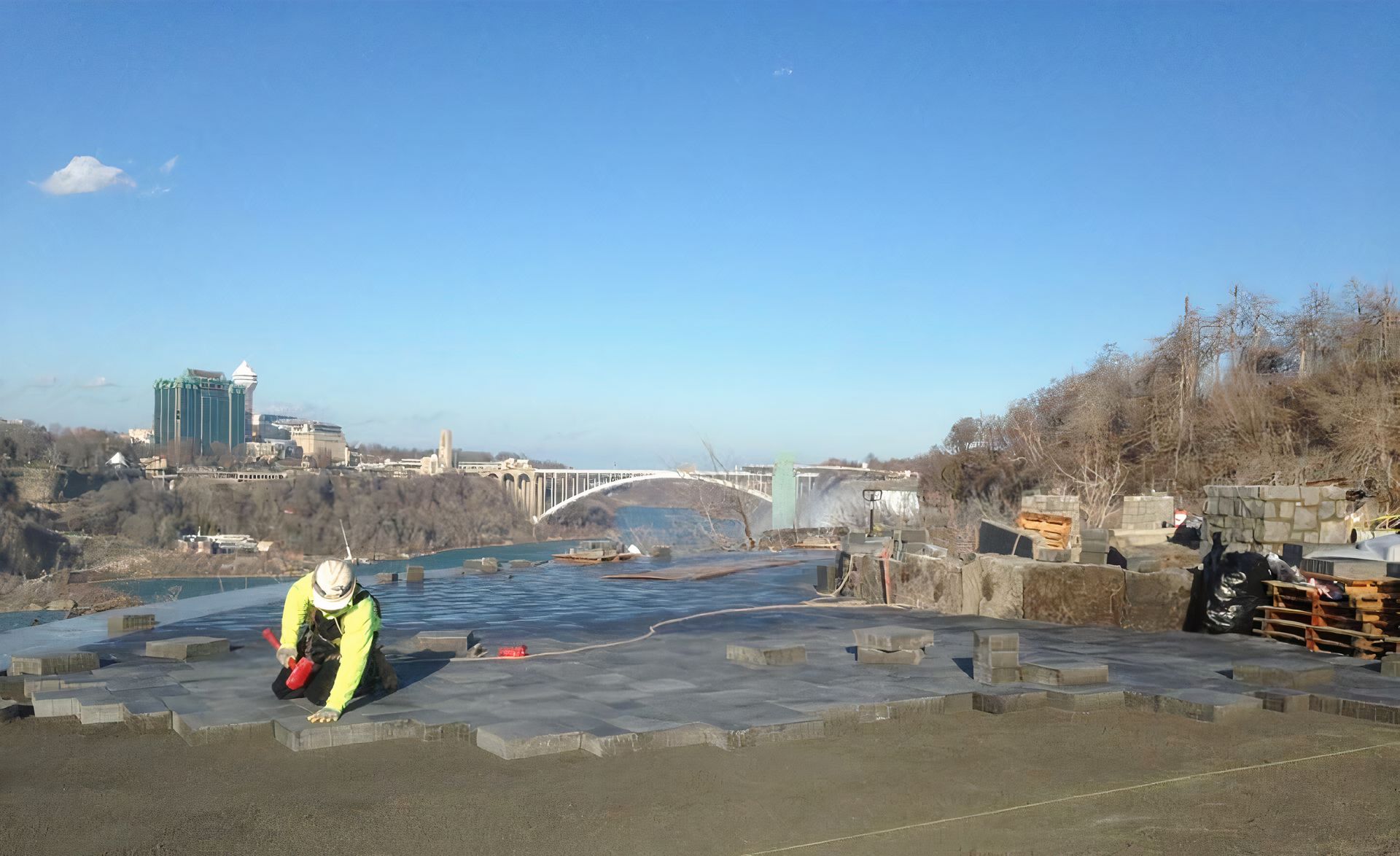 A man is kneeling on the ground in front of a river.