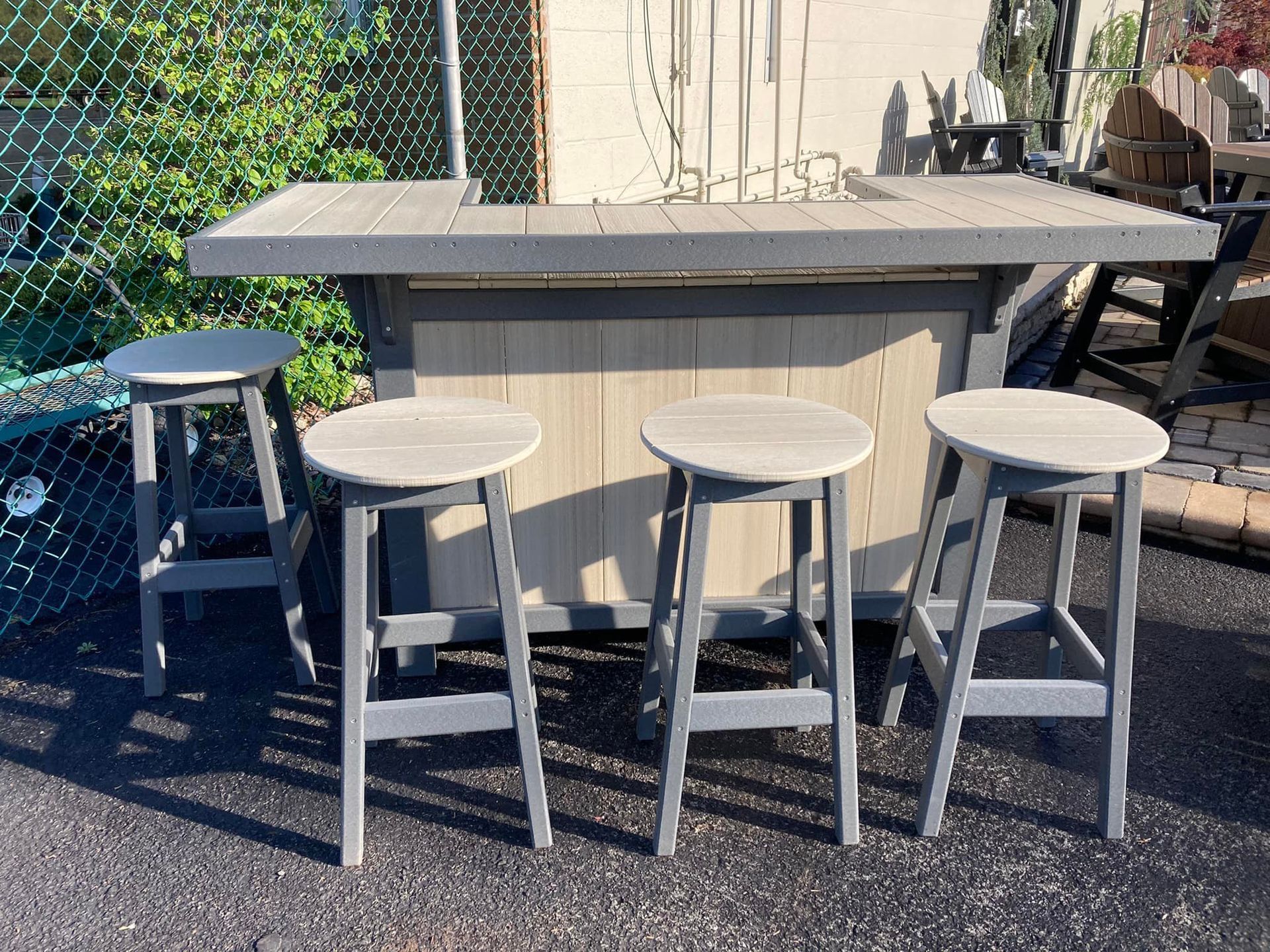A bar with four stools is sitting on the ground in front of a chain link fence.