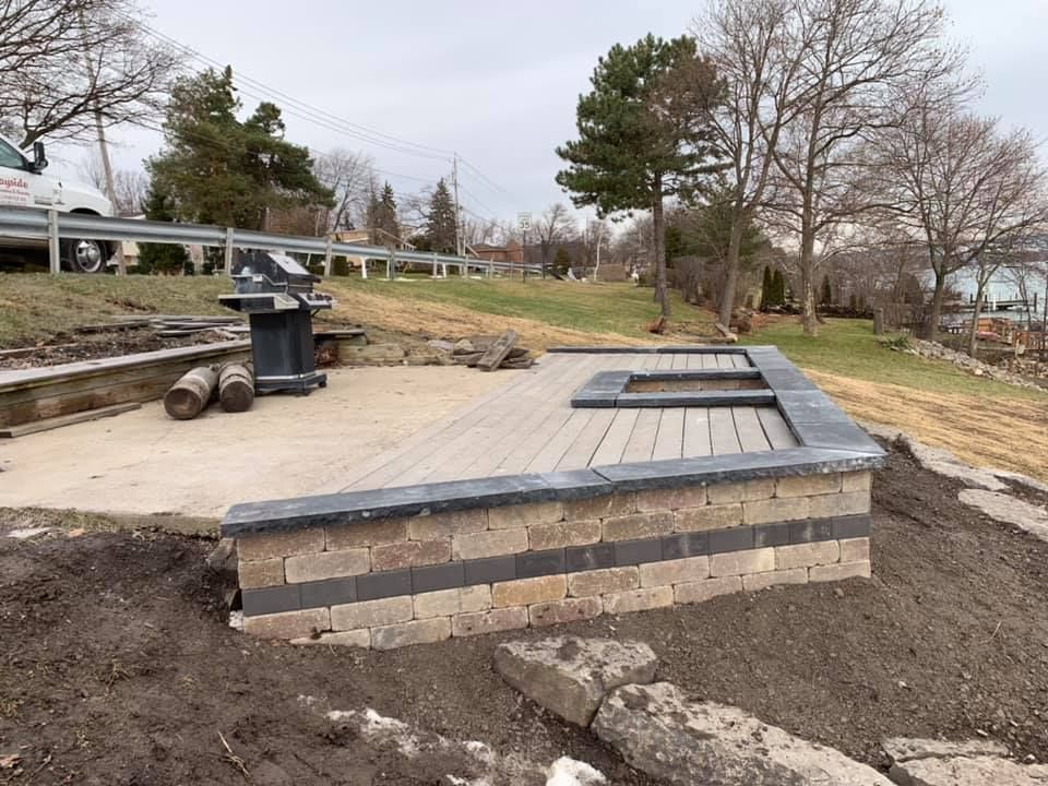 A bbq grill is sitting on a wooden deck next to a brick wall.