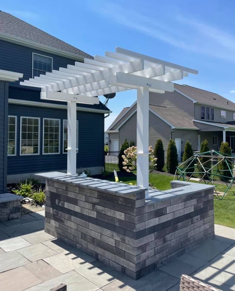 A white pergola is sitting on top of a brick patio in front of a house.