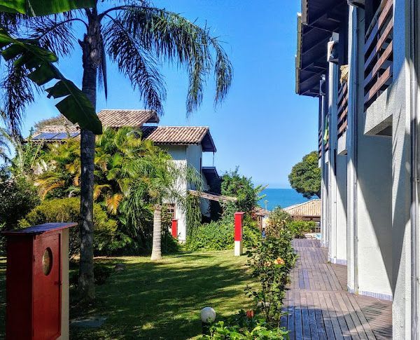 Gramado verdejante com prédios, árvores e o oceano ao fundo, sob um céu azul brilhante.