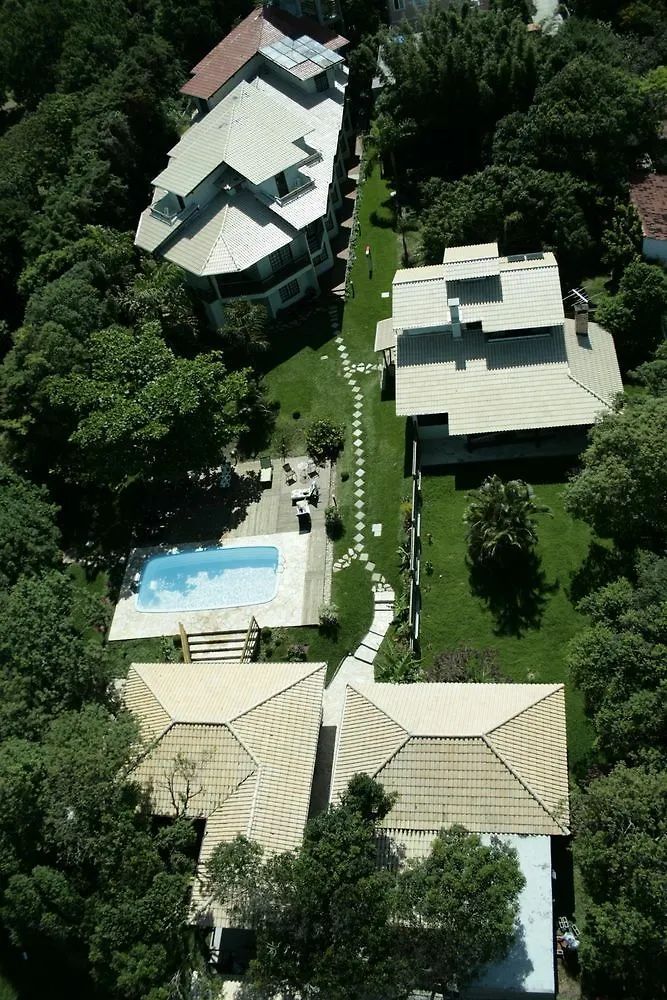 Vista aérea de várias casas com piscina, conectadas por um caminho de pedra, cercadas por árvores.
