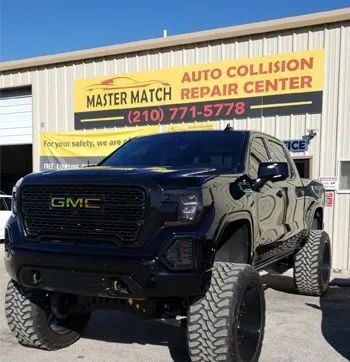 Black lifted GMC truck parked in front of an auto repair shop with a yellow and black sign.