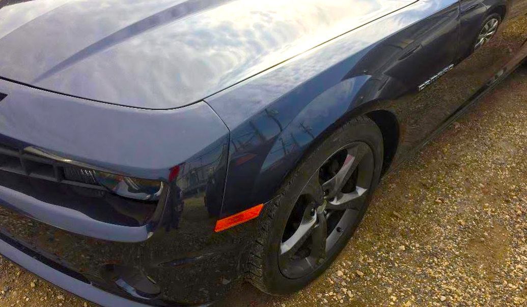 A black car is parked on a gravel road.