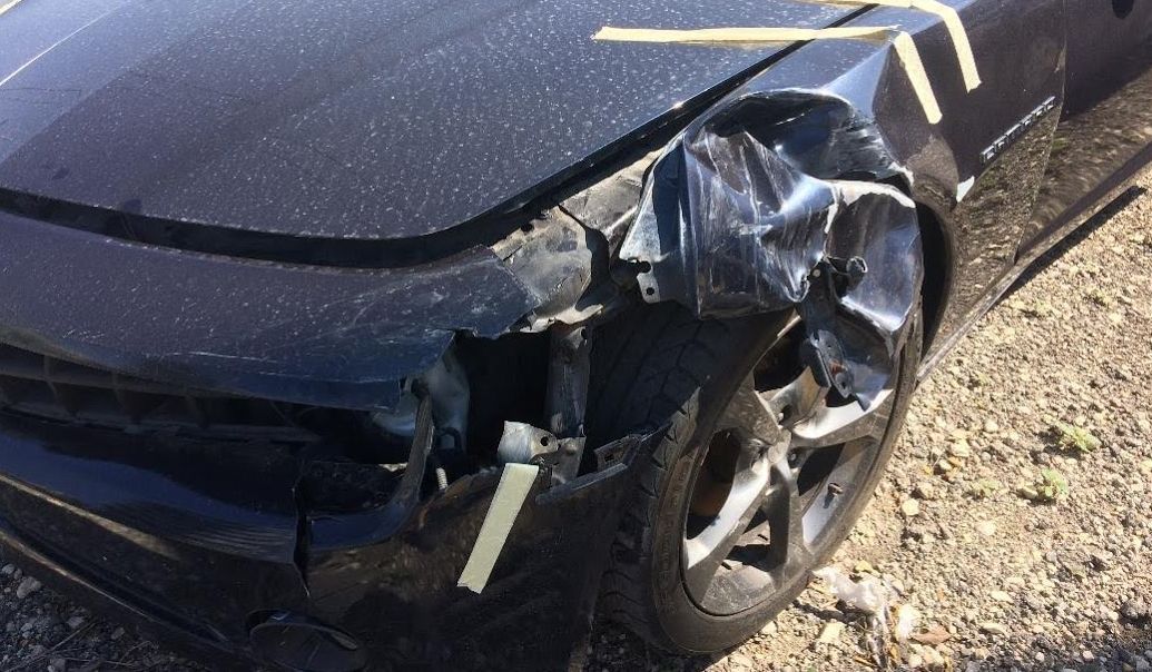 A black car with a damaged front bumper is sitting on the ground.