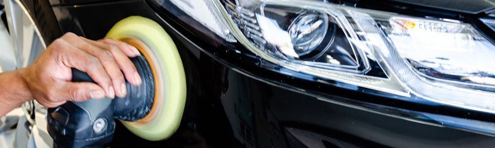 A person is polishing the headlight of a car with a polisher.