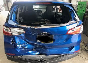 A blue car with a broken windshield is parked in a garage.