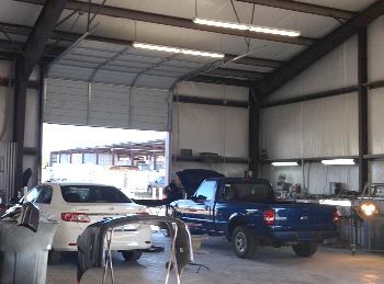 A blue truck is parked in a garage next to a white car