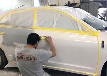 A man in a master match shirt is painting a white car.