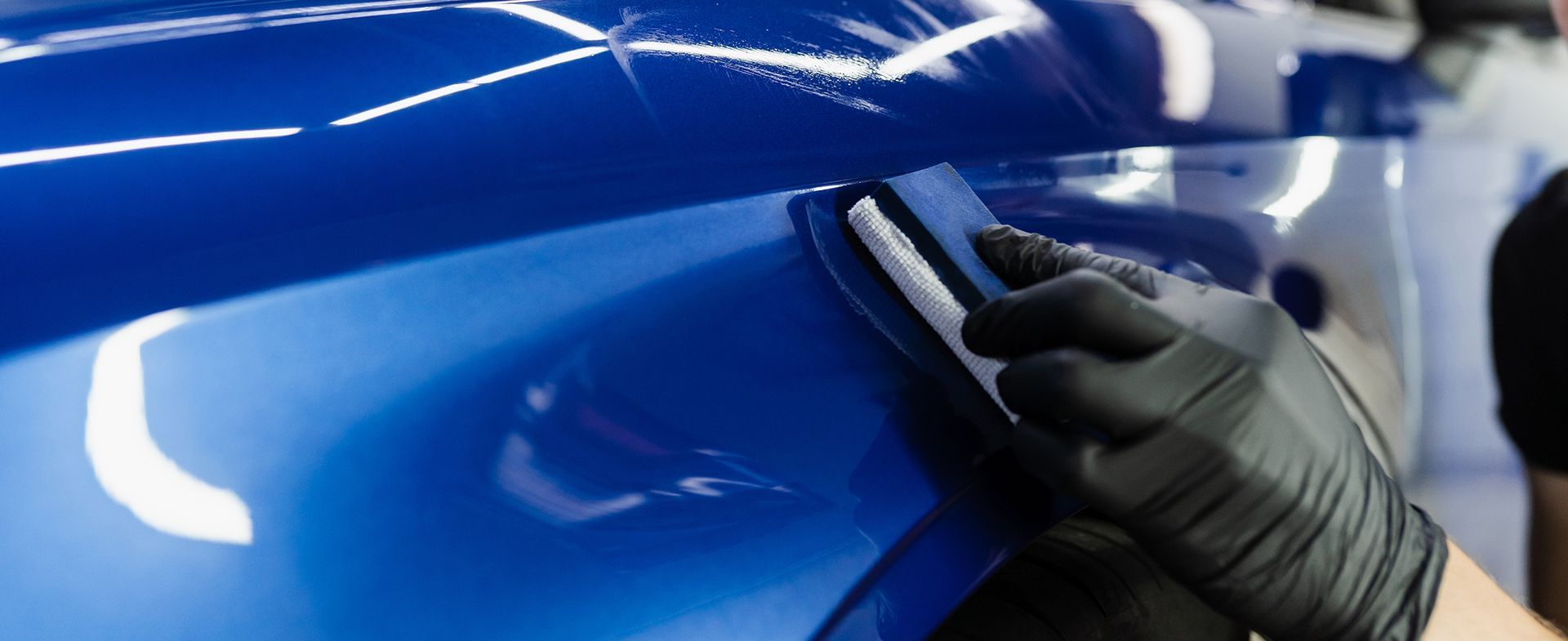 A person wearing black gloves is polishing a blue car.