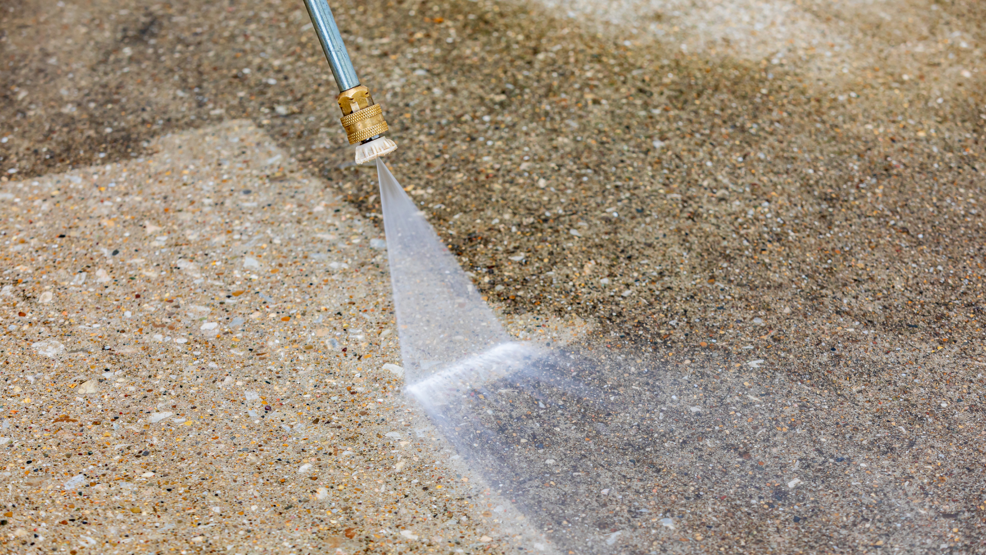 Water spraying from a blue hose nozzle onto a sandy surface