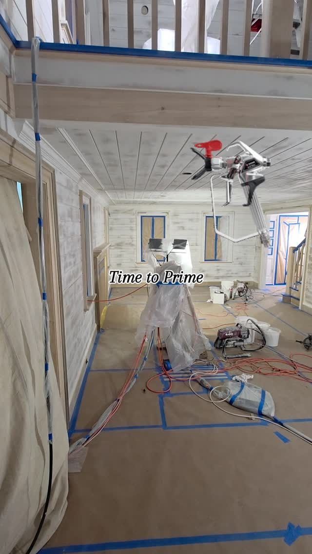 Interior construction site with blue tape outlines on floor, exposed walls, tools, and hanging work light.