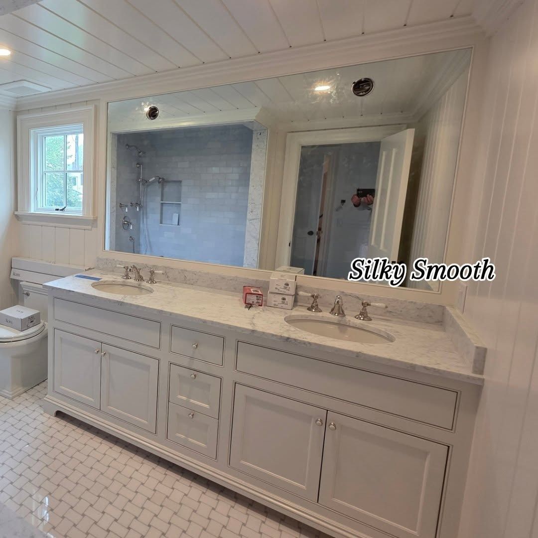 Bright white bathroom with double vanity, large mirror, tiled floor, and window by the tub area.