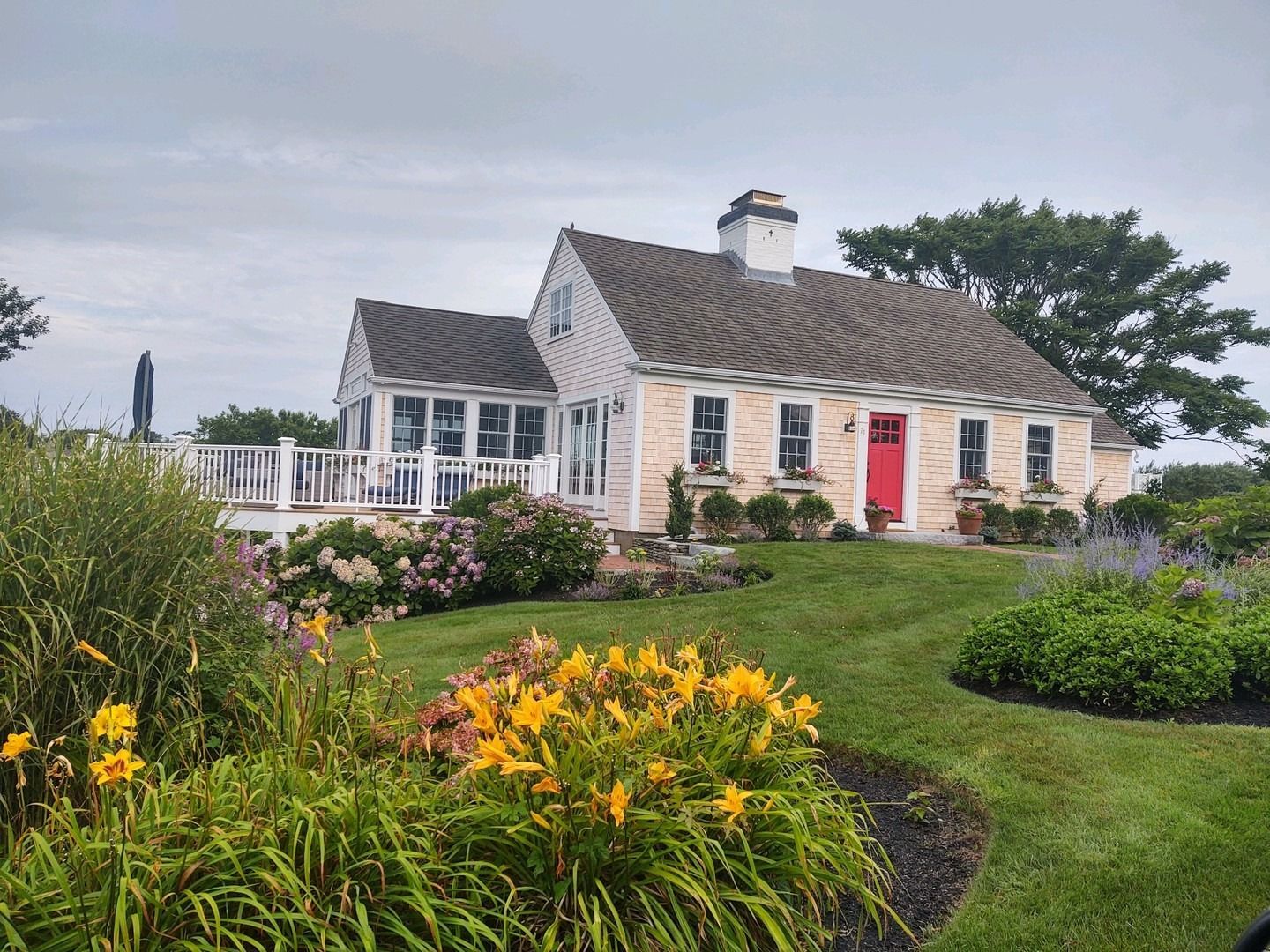White cottage with red door and garden flowers under a cloudy sky.