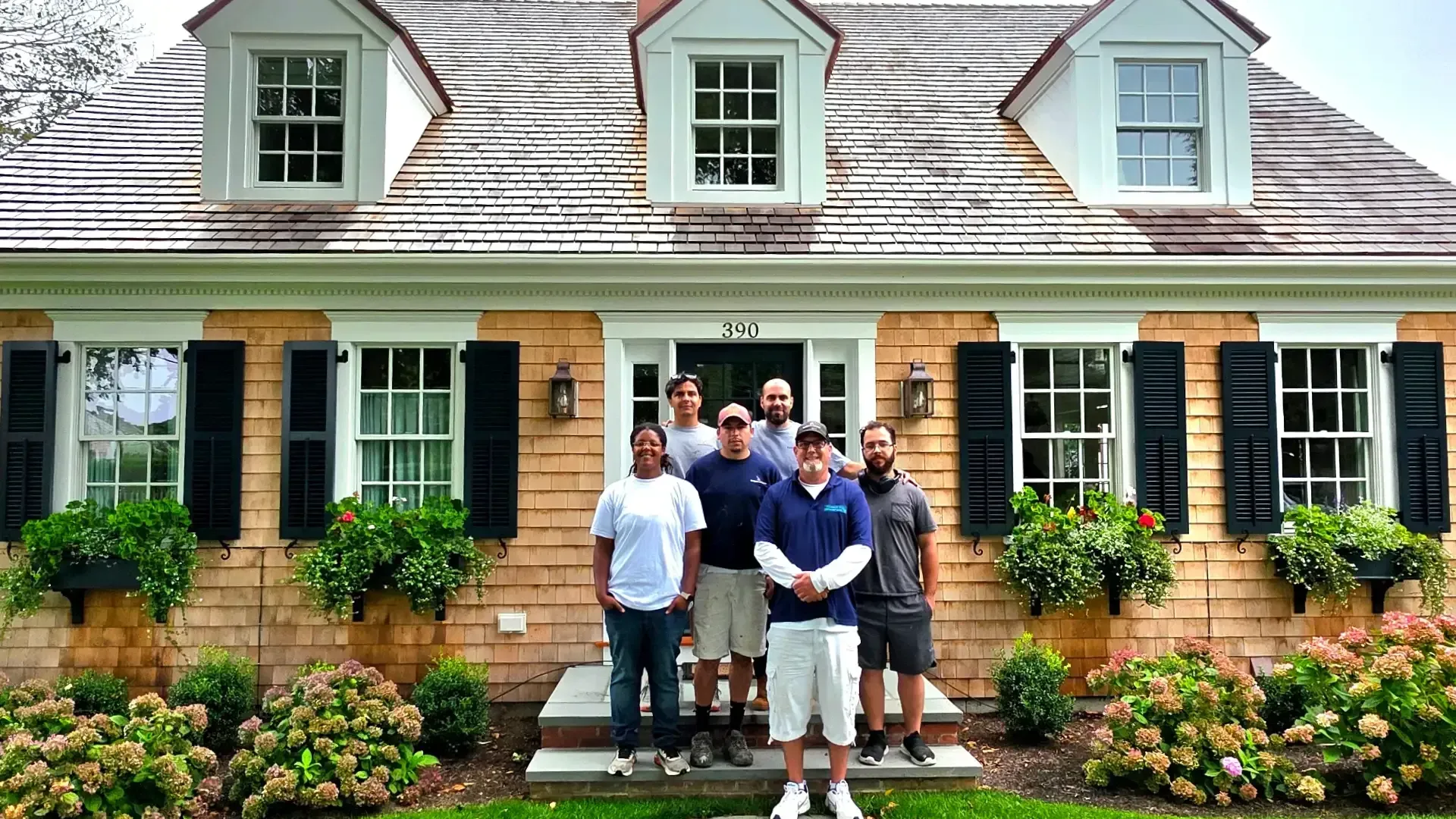 Group standing in front of a brick house with green shutters and white dormers