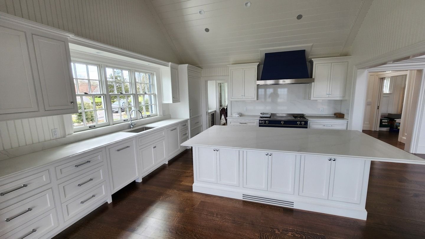 Bright white kitchen with large windows, central island, and dark wood floors