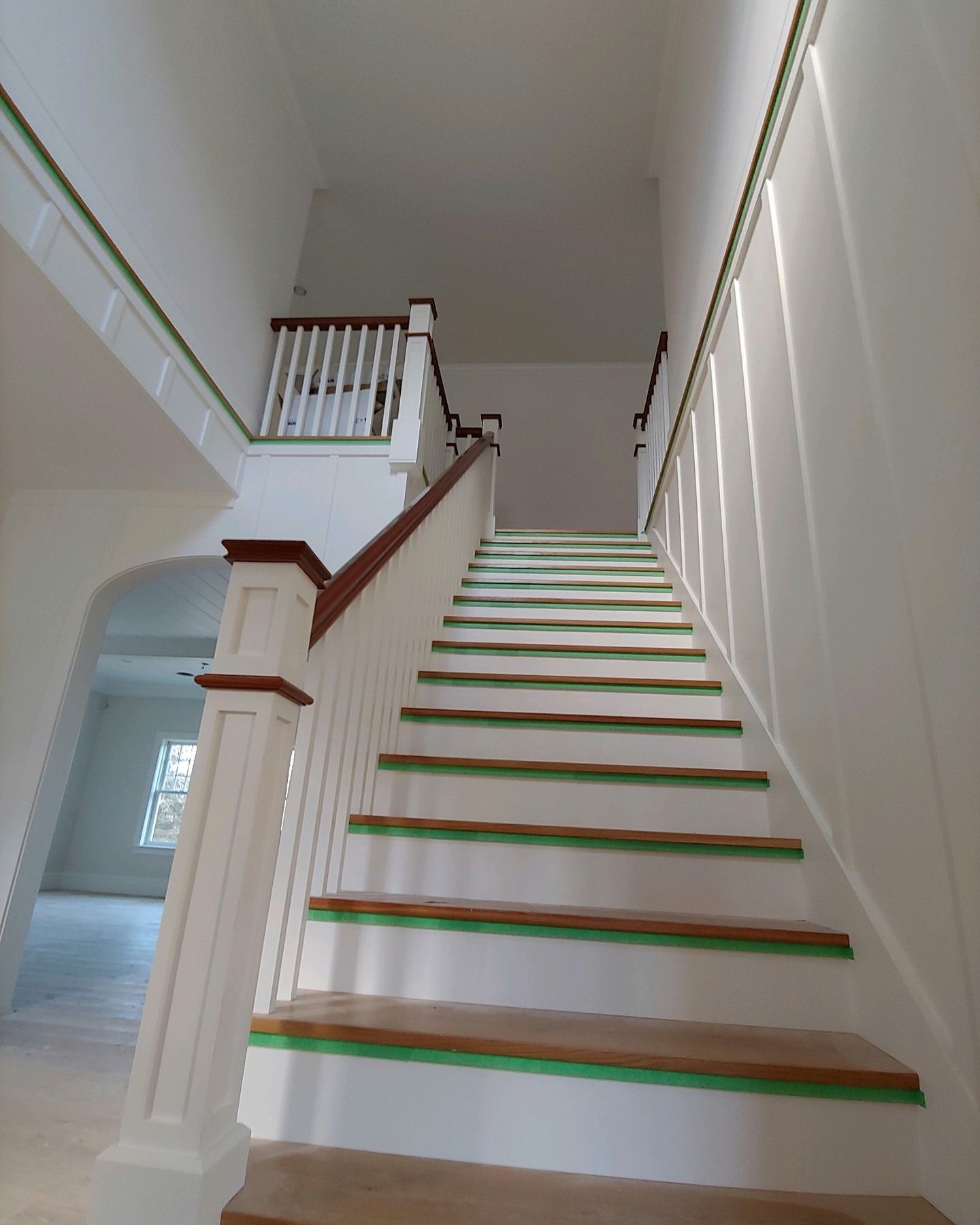 Indoor staircase with white walls, wood railings, and green-edged steps leading to an upper landing